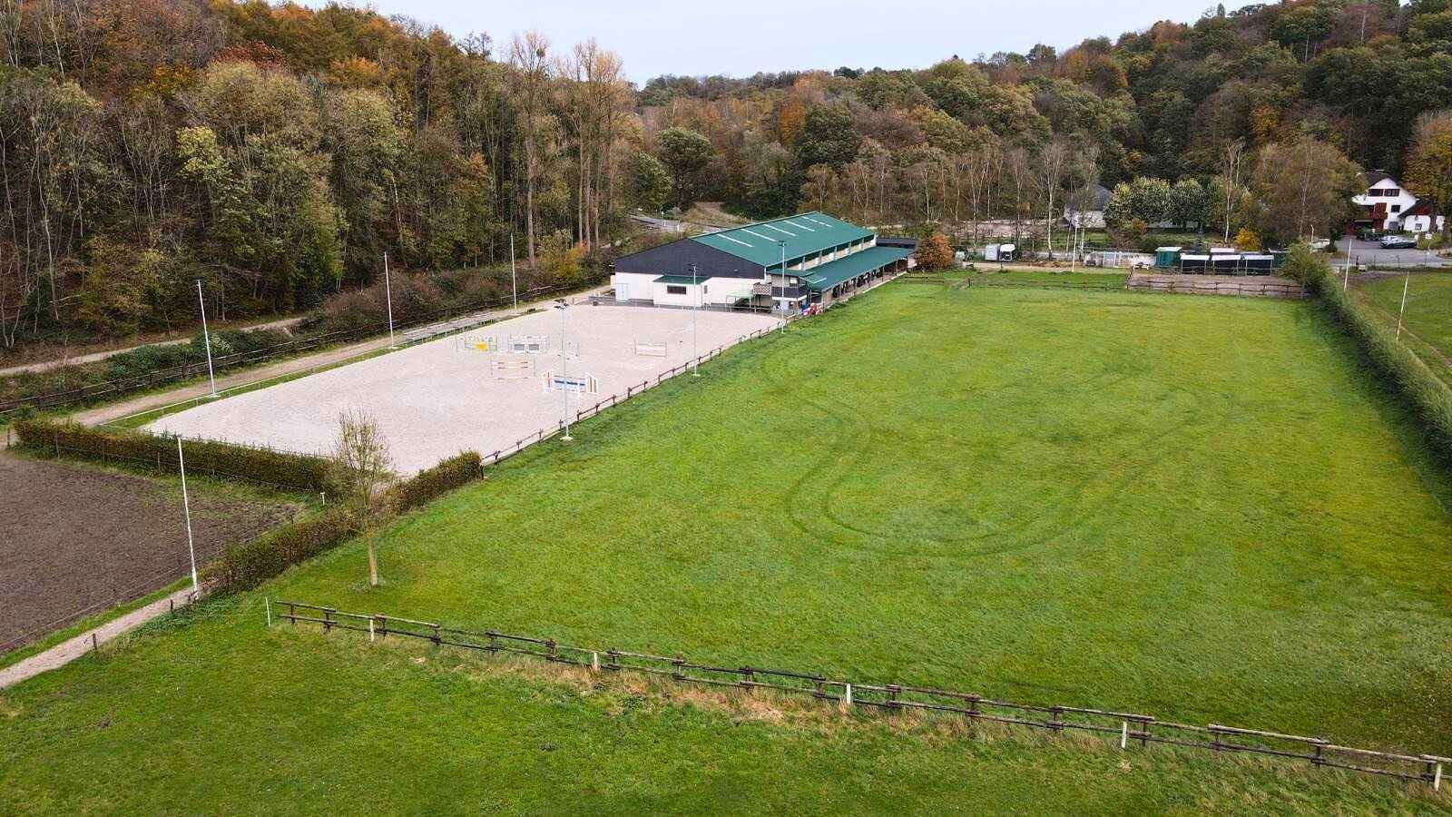 Eine Drohnenaufnahme des Teuterhofs, die den Stall von hinten zeigt. Der Außenreitplatz und die Stallgasse sind gut erkennbar.