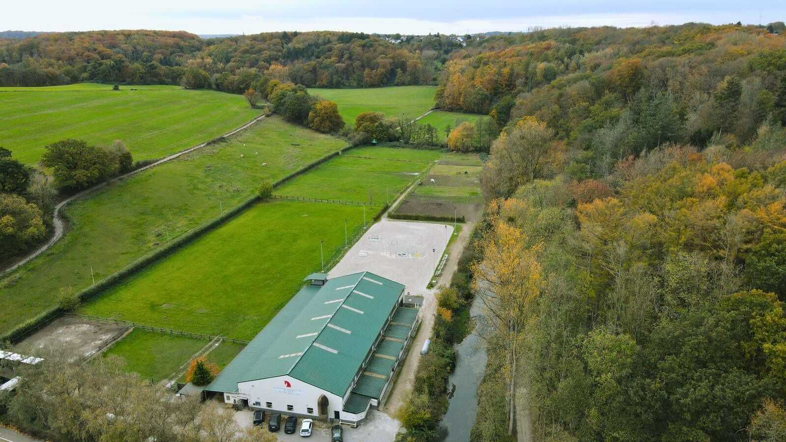Drohnenaufnahme des Teuterhofs. Der Reitstall inkl. Außenreitplatz inmitten von Wiesen und Wäldern.